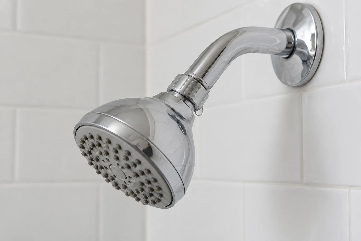 Chrome shower head with a small water bead at the connection to the shower arm.